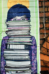Person wearing glasses and holding a tall stack of books
