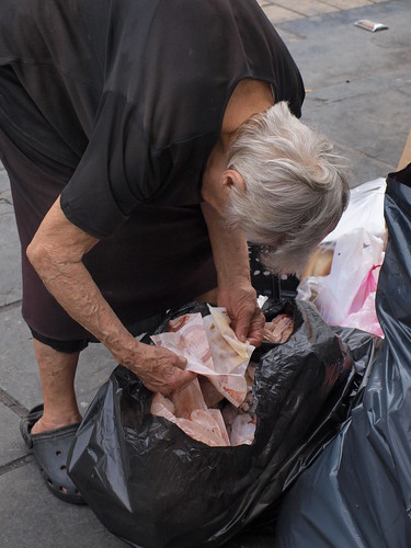 Greek pensioner looking through rubbish for leftover food