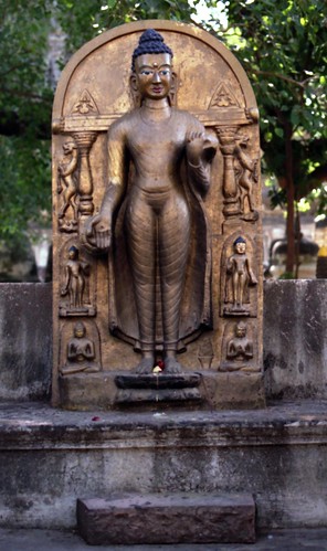 Gold painted concrete statue of standing Buddha in varada-mudrā mudra, holding his robes, with standing lions, 5 Buddhas, columns, offerings on lotus, near where Buddha gained enlightenment, BodhGaya, H.P., India in 1993 by Wonderlane
