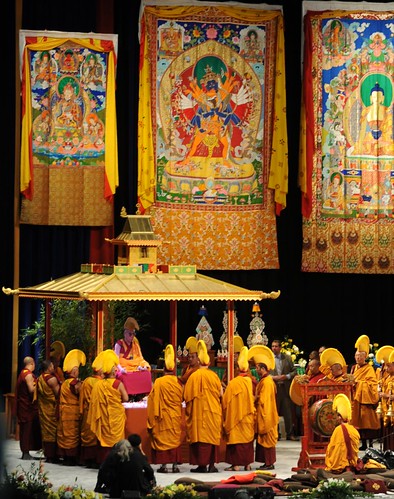 His Holiness Dalai Lama sitting on the Kalachakra mandala pavilion after dismantling the mandala, with his monks in orange robes and hats, thangkas of Padmasambhava, Kalachakra, and Lord Buddha, drum, torma offerings, Verizon Center, Washington D.C., USA by Wonderlane
