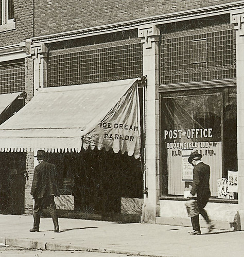 people usa signs man men history cars buildings walking advertising awning clothing mail postoffice indiana streetscene transportation shops pedestrians storefronts automobiles businesses bloomfield greenecounty realphoto hoosierrecollections