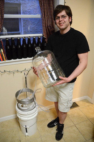 Temple student Jake Daly-Leonard stands in his West Philadelphia home holding his secondary fermenter. Daly-Leonard recently finished brewing a jalapeno beer from a recipe from Home Sweet Homebrew owner George Hummel's book.
