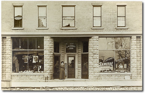people woman usa signs man men history sepia buildings advertising clothing women drugs shops storefronts businesses fultoncounty realphoto kewana hoosierrecollections