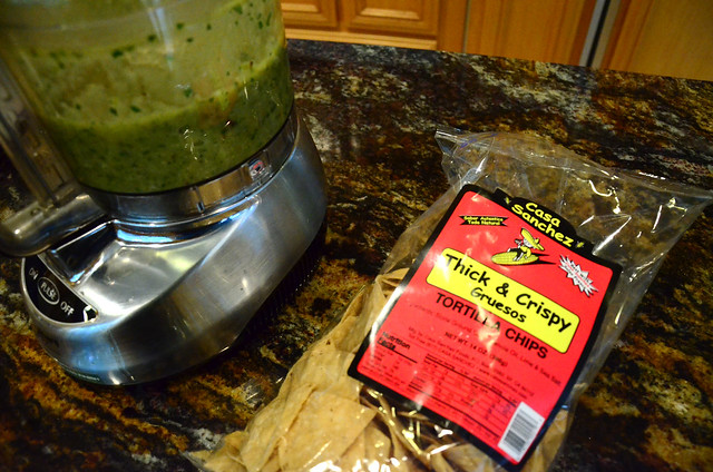 A food processor with the finished salsa inside next to a bag of chips.