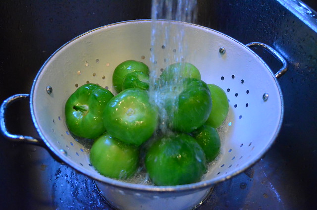 Tomatillo inside a colander with their husks removed being washed in a sink.