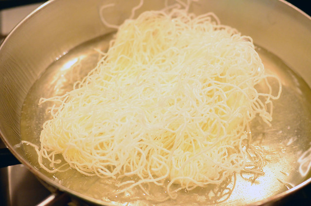 Rice stick noodles being fried in a large frying pan.